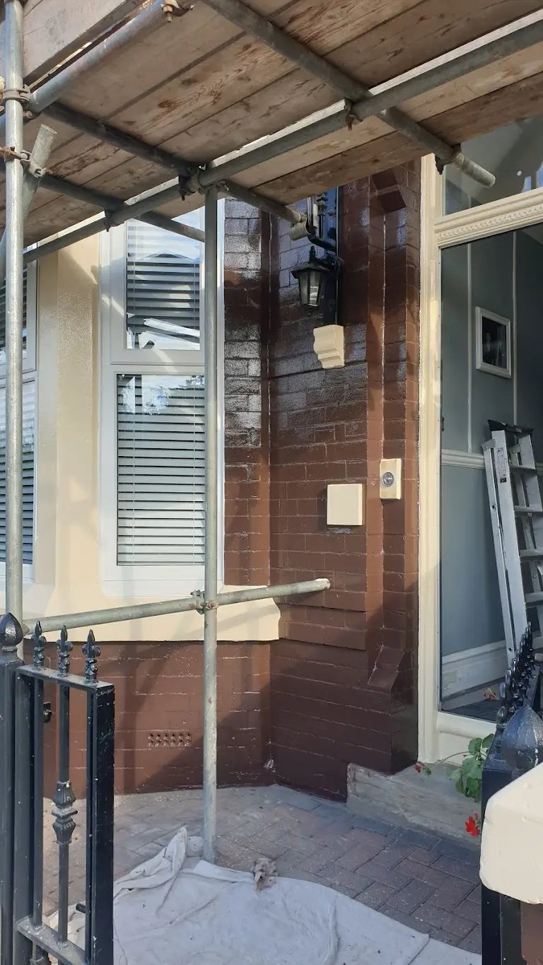 Decorator painting the front of a terraced house from scaffolding
