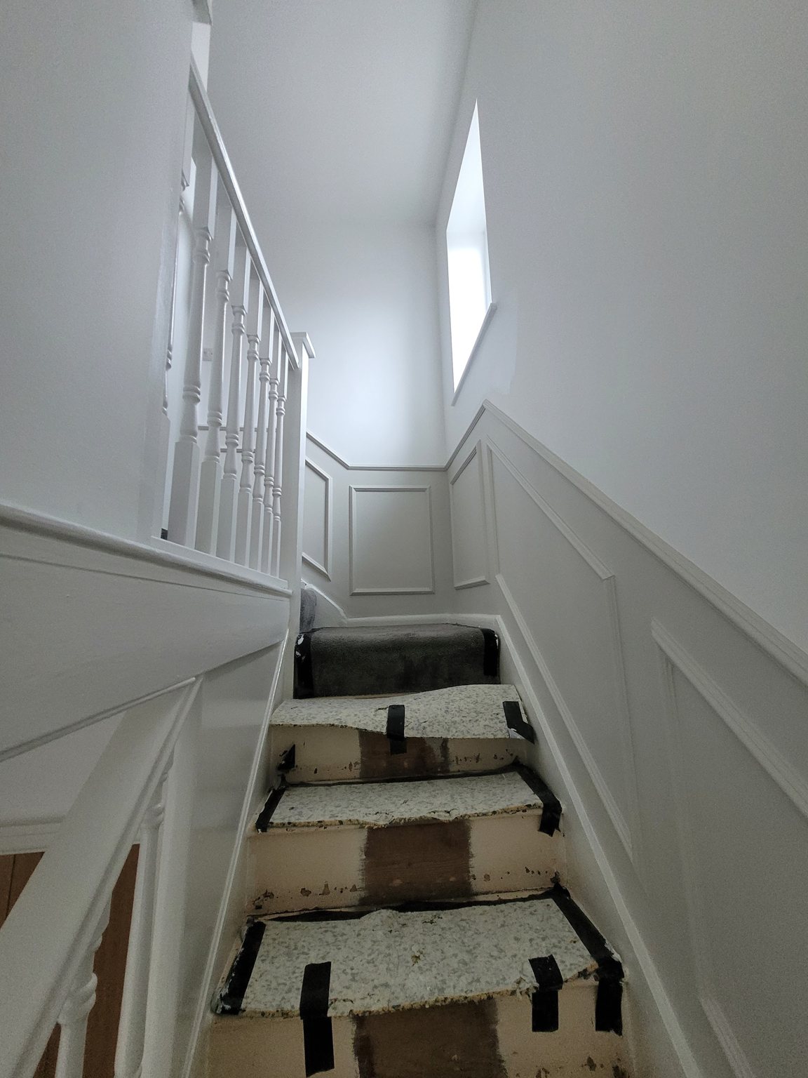 Staircase with white wall panelling and freshly painted spindles