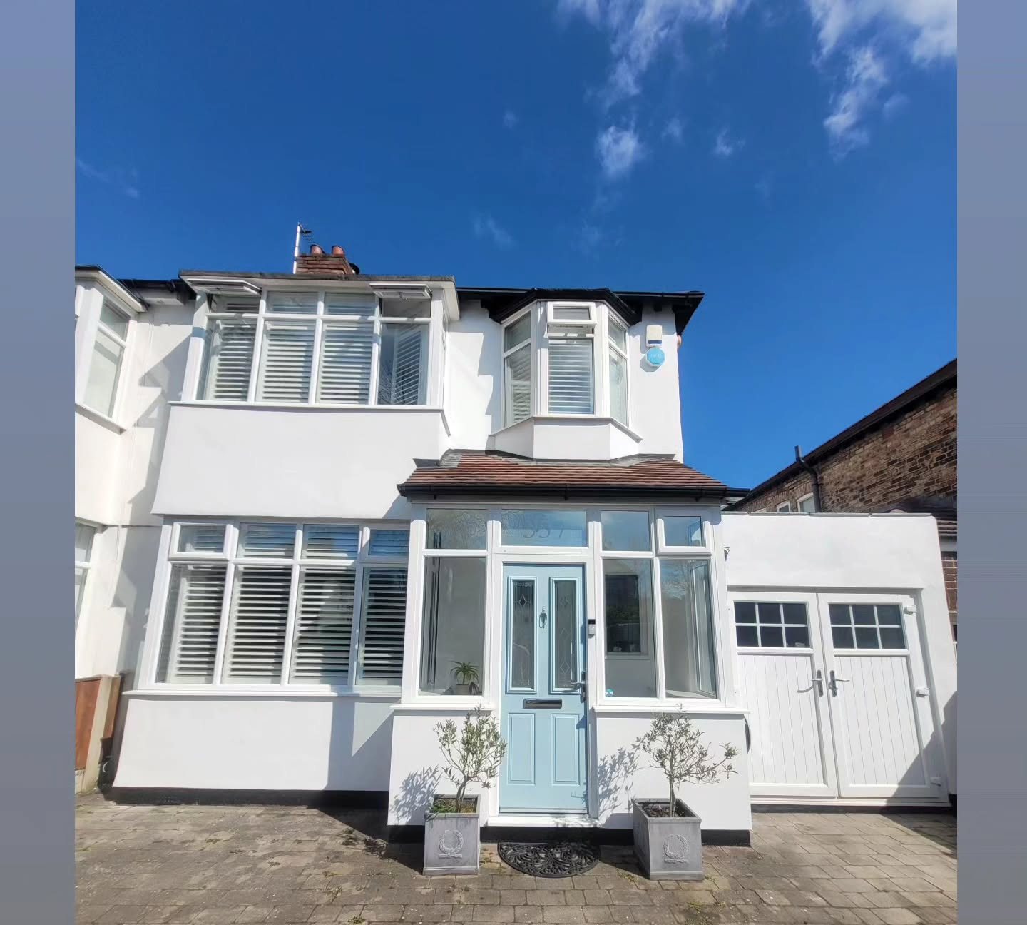 White semi-detached house with a pale sage front door under blue sky